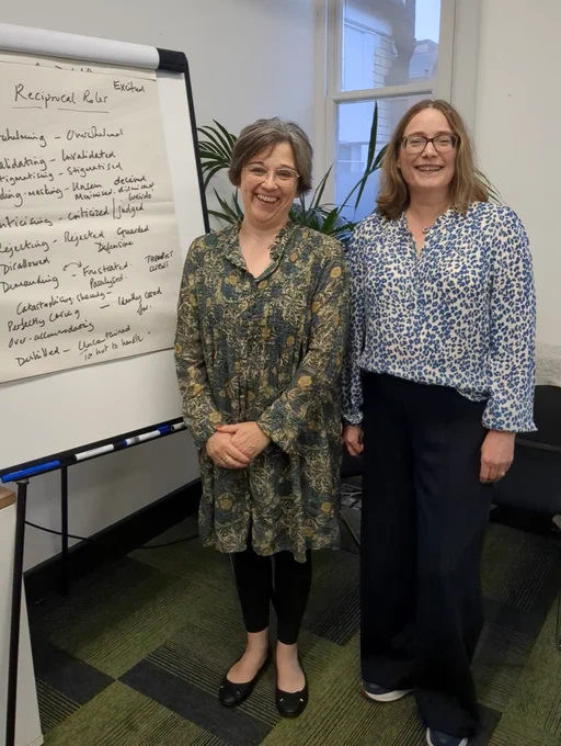 Two smiling women next to a flipchart stand with writing on it from a group exercise.