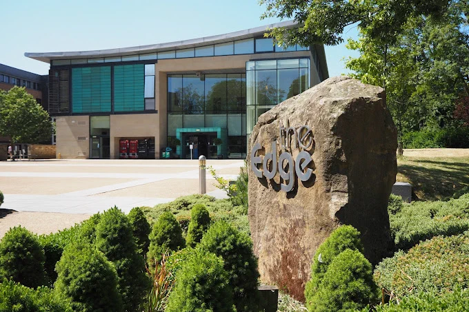 A wide-angle view of The Edge conference centre in Sheffield, a modern building with large glass windows, set against a backdrop of greenery and an open sky.