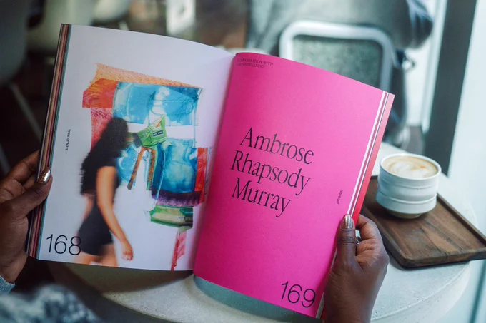 A photo of the journal opened to a spread with an illustration and a page with a pink background and text that says “Ambrose Rhapsody Murray.”