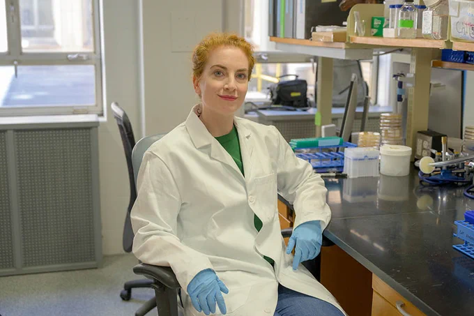Catherine Armbruster sits in her lab and smiles at the camera.