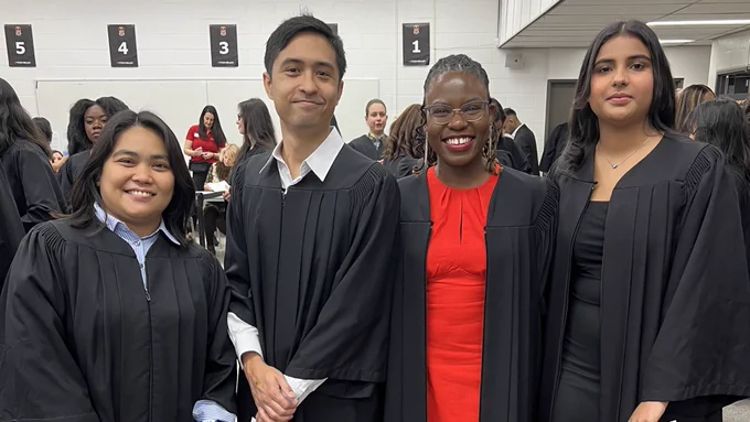 Four graduates smiling at the camera wearing their gowns.