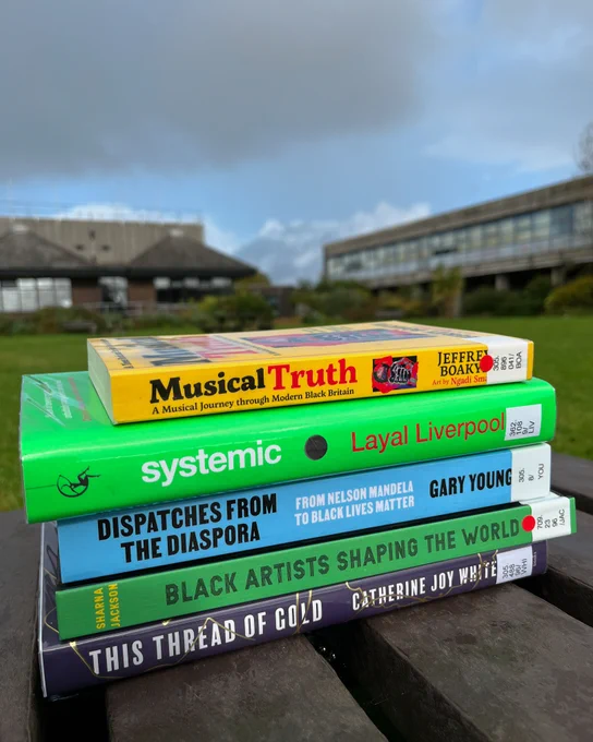 5 books by Black British writers in a pile, with their spines facing out, on a bench in the Plymouth Marjon University quad.