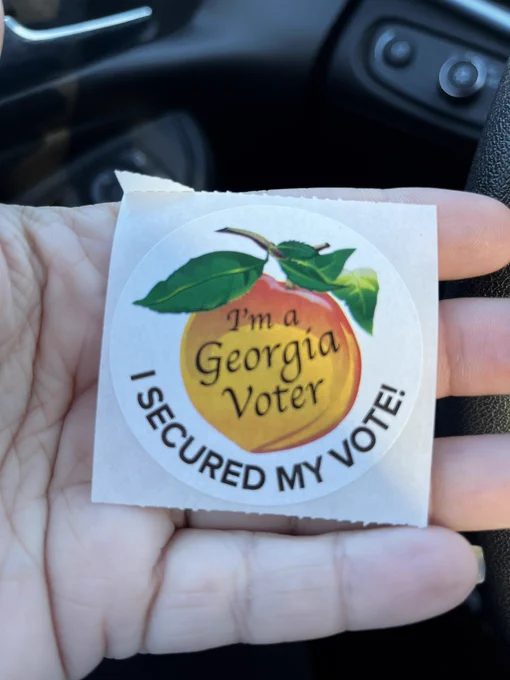 Photo of “I’m a Georgia voter. Secured my vote!” sticker with a Georgia peach in the palm of a hand