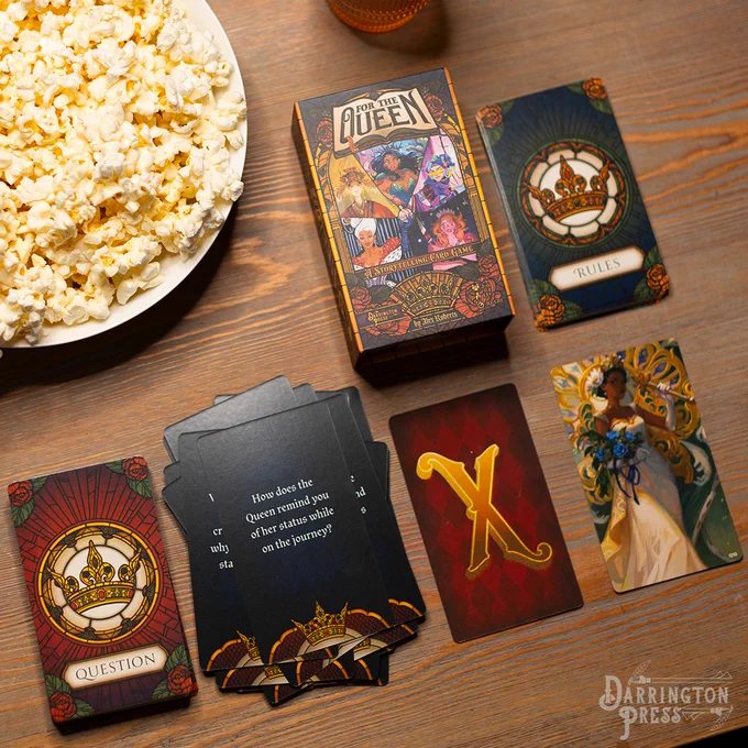 Darrington Press's collaborative storytelling game For the Queen. Game is displayed mid game on a wooden table with popcorn and a drink.  