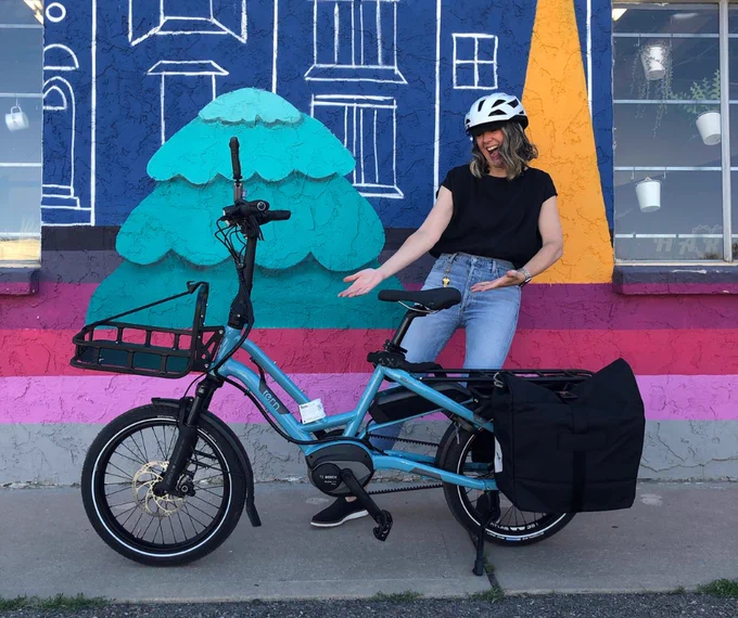 Person showing off their blue e-bike, parked in front of a colorful mural featuring abstract designs.