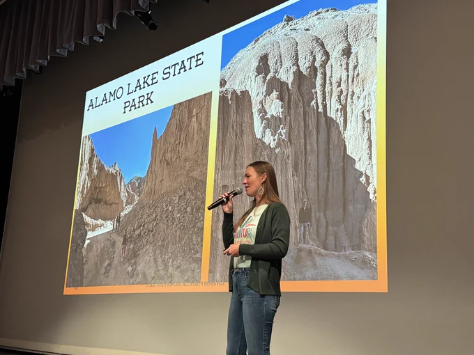 Woman with microphone on stage and image of mountain in background.