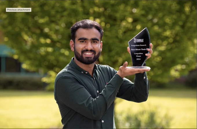 Man smiling holding a trophy standing in outdoor setting