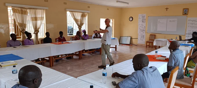 A volunteer in the middle of a classroom speaking to co-op members. The co-op members are seated in desks and these desks are in a horseshoe position.