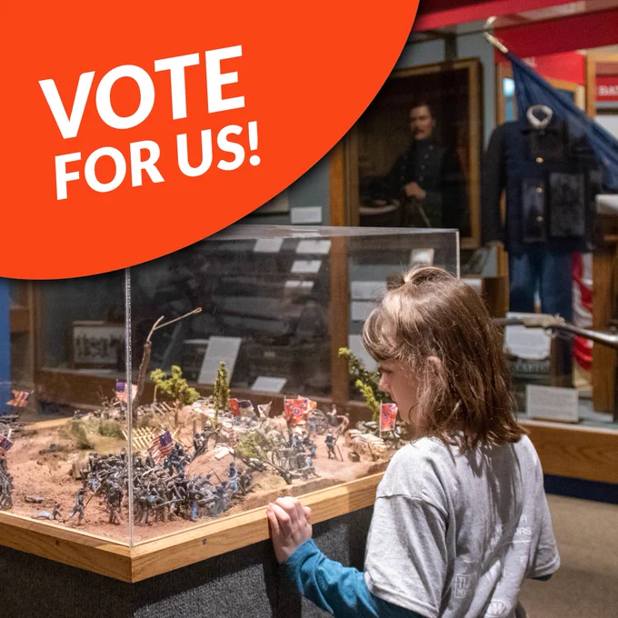A young girl looking at model soldiers in the Civil War gallery. Top left corner has a bright orange circle that says "Vote for us!". 