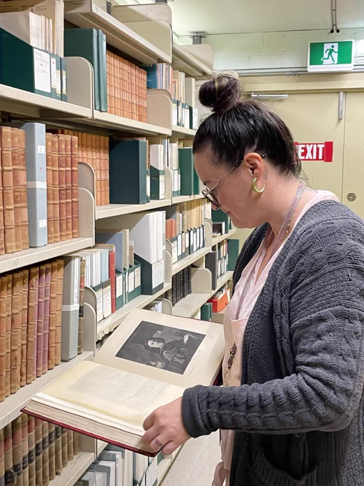 LAC employee holding an open book with a bookcase in front of her.