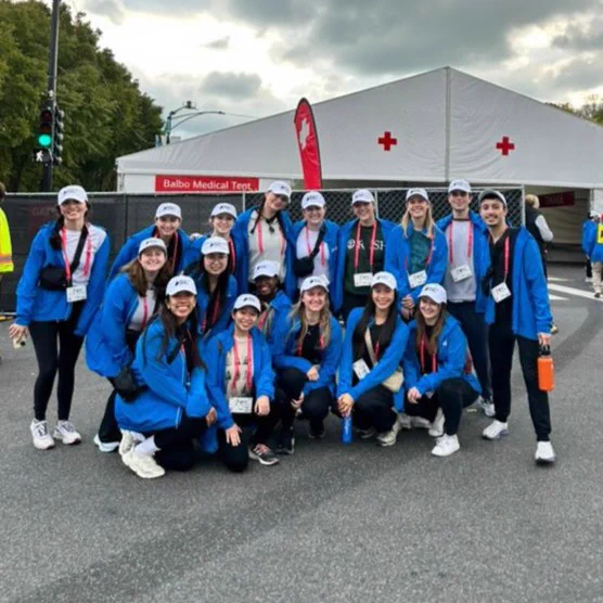 Group of Rush PA student volunteers wearing blue jackets and white caps standing in front of a medical tent at the Chicago Marathon.