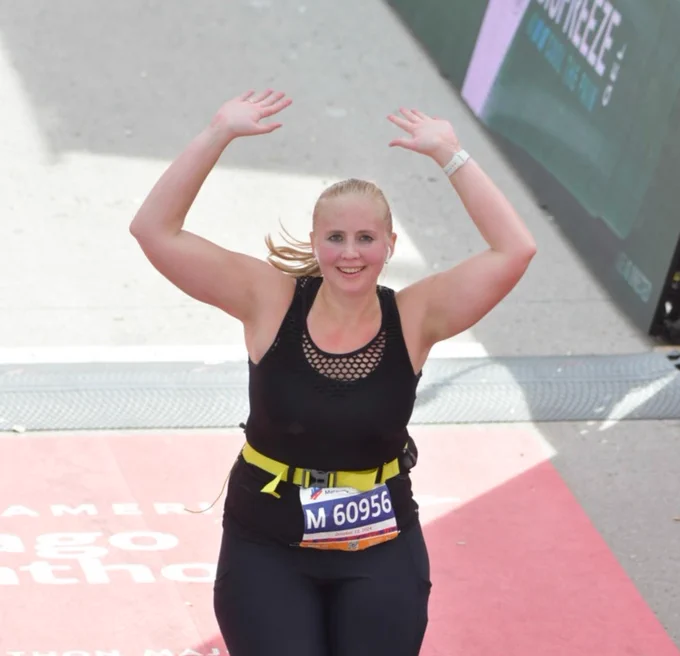 Rush Medical College student crossing the finish line at the Chicago Marathon, arms raised in a victory gesture.