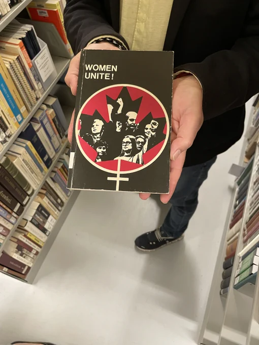 Hand holding a book with a black cover and small circular graphic featuring women with their fists raised entitled "Women Unite."