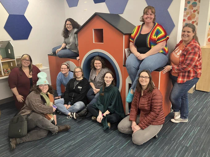 Smiling women pose around a red playhouse.