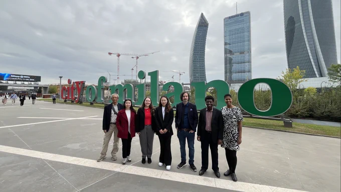 Members of Team Space Enabled pose outdoors in front of a red and green "city of milano" sign. 