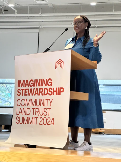 Michelle Cooper Iversen stands behind podium speaking at Community Land Trust Summit 2024.
