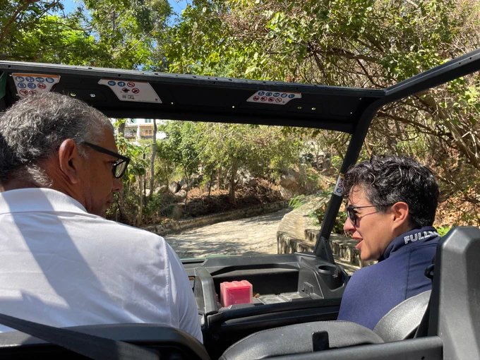 Dení López in the passenger seat of a vehicle with a man driving
