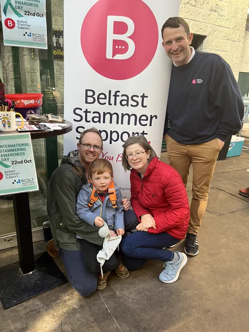 2 adults crouching down with toddler and one adult standing smiling in front of pop up