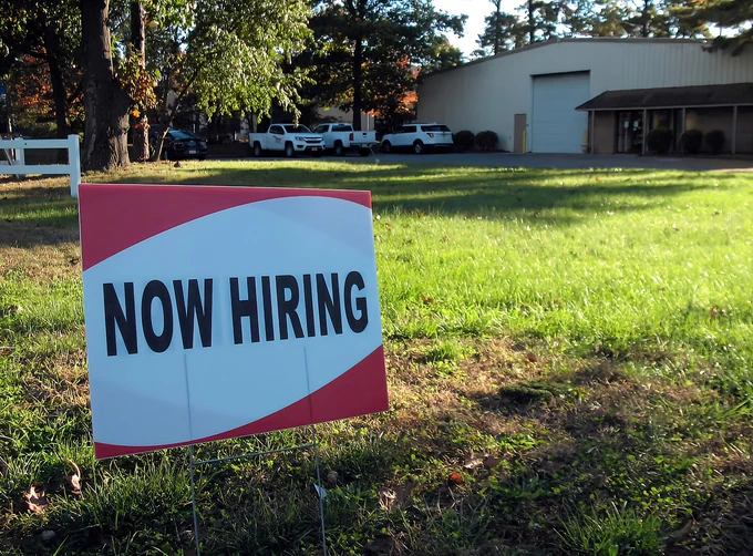 a now hiring sign in front of a building

