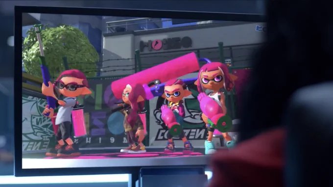 A team of four pink Inklings stand on a spawn point as a player looks at the screen, from the Nintendo Switch reveal trailer
