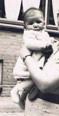 Vintage black and white photo of a woman holding a baby in front of a brick building.