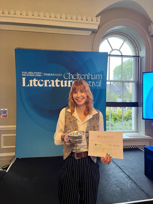 Holly Lovelock, Development Officer for Libraries, who is project lead for the winning library initiative, holding the prize and a certificate in front of a board saying Cheltenham Literature Festival