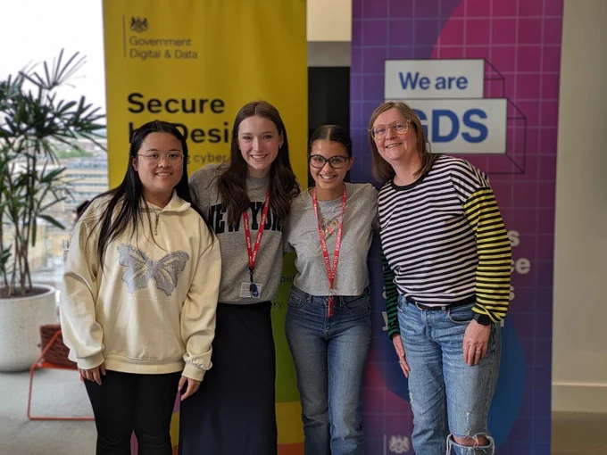 Lead Designer at GDS, Dr Sarah Kirby-Ginns, is standing with the three Next Tech Girls placement students.

They are stood in front of the GDS roll up banners that say: “We are GDS”.