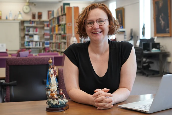 a researcher sits with a statue of Mary with a laptop in the Marian Library