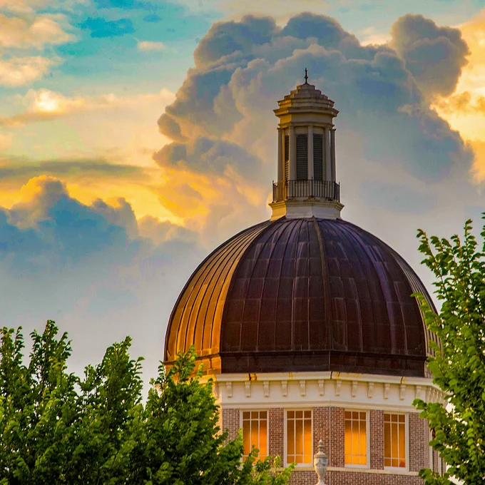 A view of the top of the Aubrey K. Lucas Administration building at sunset, surrounded by trees.
