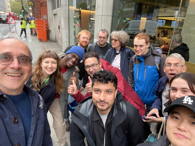 A group of people smiling for a selfie outside a Starbucks in London, ahead of a Stammering Pride / STAMMA Starbucks Day of Action. 