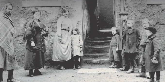 Photo of a group of women and young children in the early 20th century in a working class city street