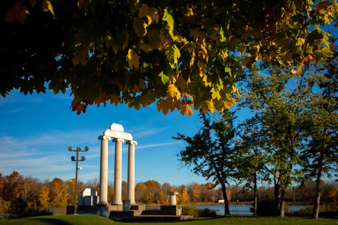 Baird Point stands against a vibrant blue sky and an early fall tree line. In the foreground is a tree with leaves starting to turn for the season.