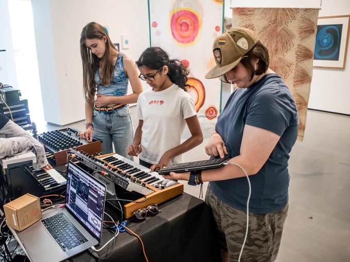 Three young people performing at a WIRED event, playing vintage synths and a MIDI controller.