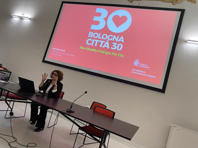 The Deputy Mayor of Bologna presents in front of a large screen showing the red and white logo ‘Bologna Citta 30’.