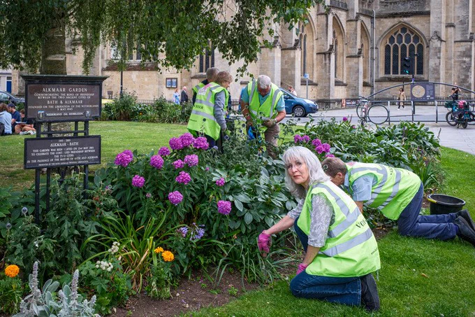 Volunteers wearing high visibility vests working on flower beds in front of a church 