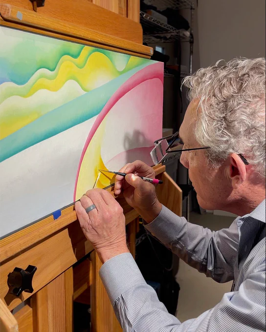 Photograph of a person with special glasses working with precise tools to repair a painting by Georgia O’Keeffe in shades of pink, yellow, and green. 