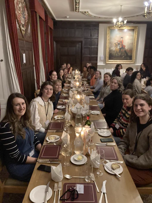 Picture of a long table set with placemats and candles with all attendees of the event on either side.  Set in the dining hall of Cumberland Lodge, Windsor.
