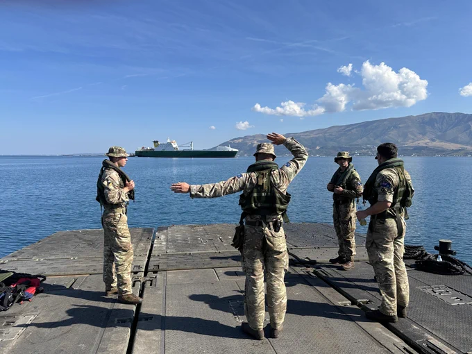 A group of soldiers wearing camouflage uniforms stand on a boat directing a boat on the horizon.