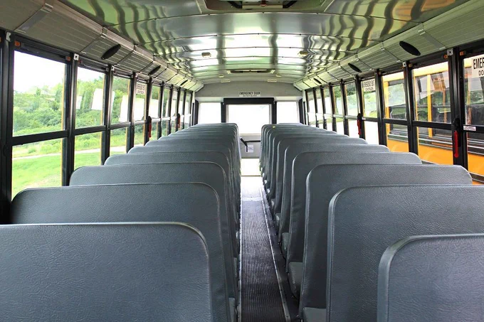Image of the interior of a school bus, the photo shows two rows of high backed seats with an aisle in the middle.