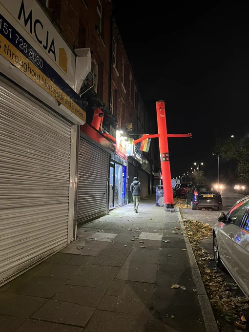 a large red tube inflatable with arms and the bongos bingo logo on the pavement outside a fireworks shop
