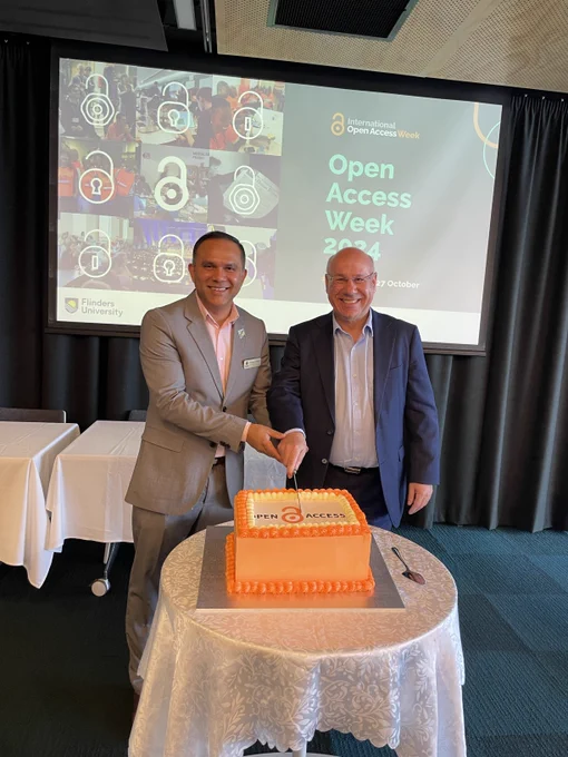 Prashant Pandey and Vincent Bulone cutting a large orange cake that says open access on it.