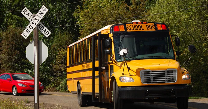 An image of a school bus stopped at a railway crossing with it's door open.