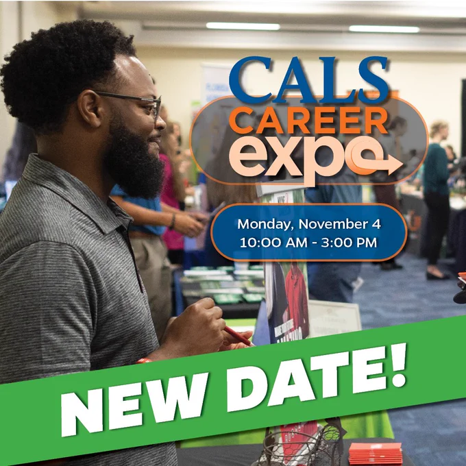"New Date!"

A man standing behind a table in a conference hall smiles at someone off screen. 