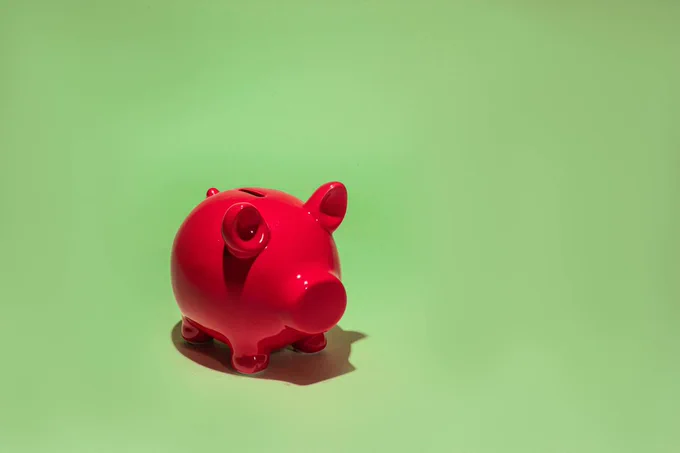 Picture of a red ceramic piggy bank on a lime green background.