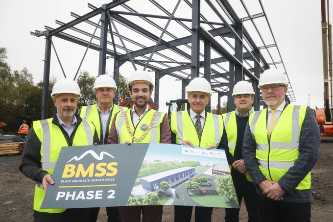 Belfast Lord Mayor Micky Murray with funders and reps from Black Mountain Shared Space at the construction site wearing high vis vests and hard hats and holding a prop with an artist impression of the new building