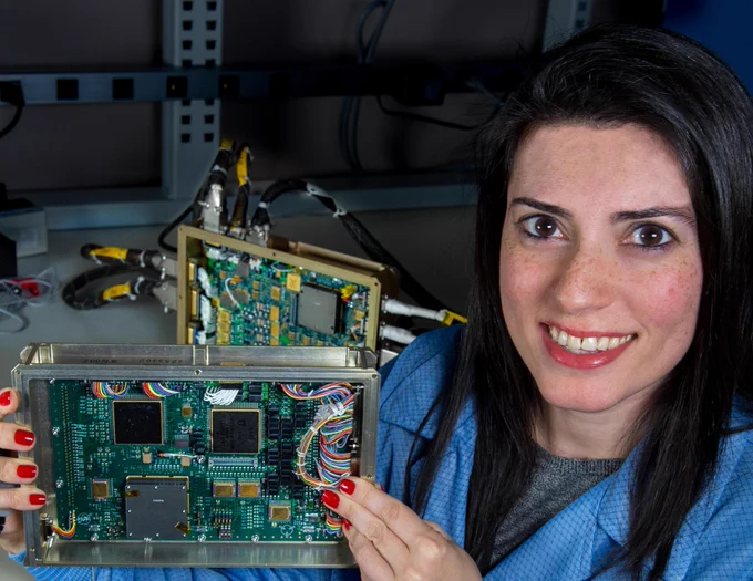 Noosha Haghani holds a piece of equipment and smiles directly at the camera. Credit: NASA