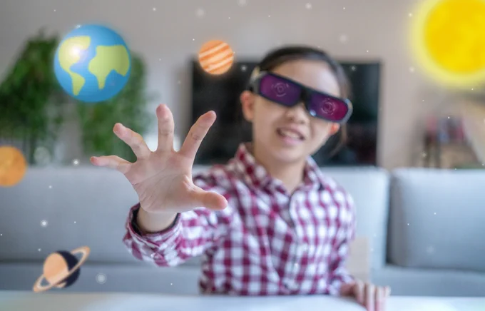 Young girl wearing virtual reality glasses and holding her hand out to visual of the solar system.