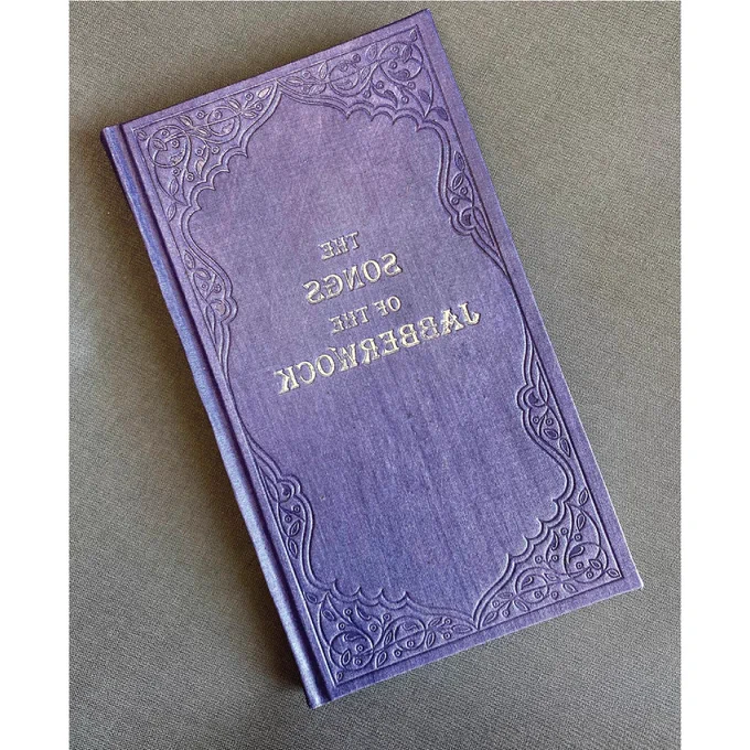 A purple hardcover book with intricate ornaments framing an embossed title that reads “The Songs of the Jabberwock” spelled in mirrored direction.