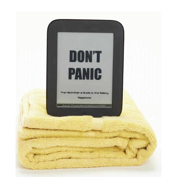 A black, digital tablet displaying the words “Don’t Panic / The Hitchhiker’s Guide to the Galaxy / Megadodo”. The tablet rests on top of a folded yellow towel.