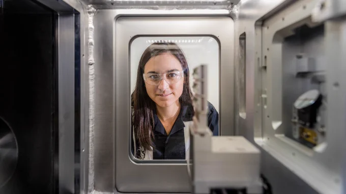 Whitney Loo (an Asian woman in a black shirt) peering through a plexiglass window in a scientific tool